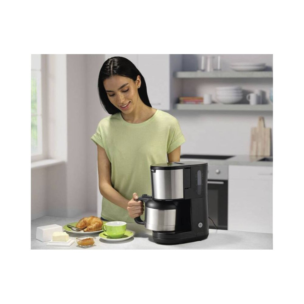 Kobieta w jasnozielonej koszulce obsługuje ekspres do kawy. Obok śniadanie.