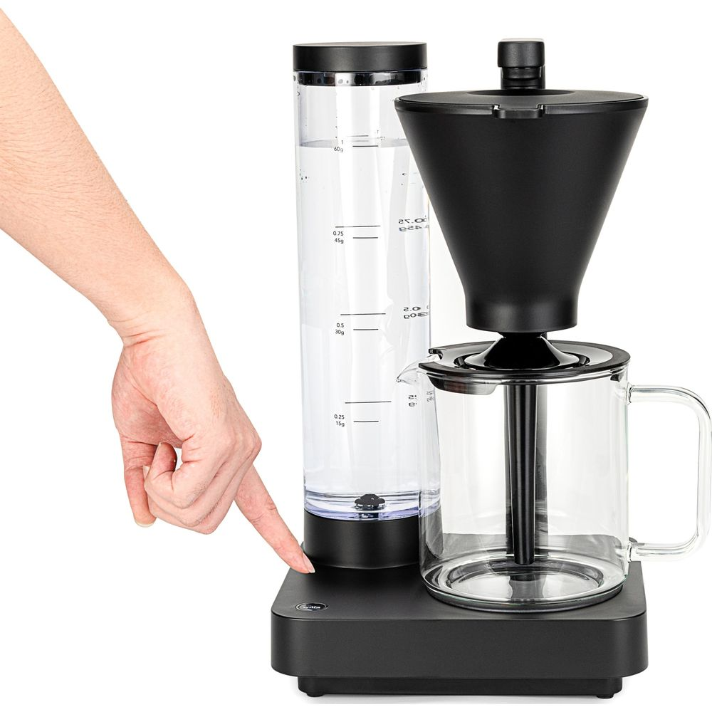 Una mano preme il pulsante di una macchina da caffè con serbatoio.