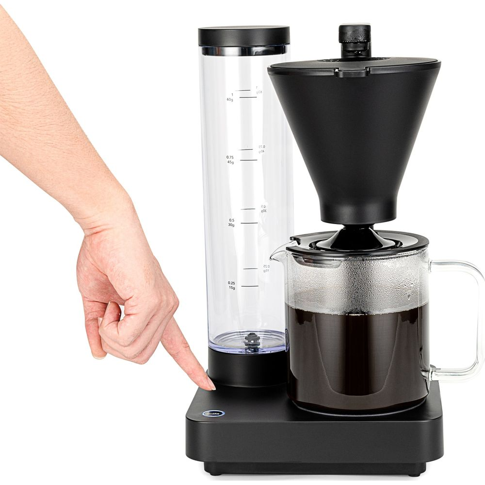 Una mano preme un pulsante su una caffettiera nera con caraffa in vetro.
