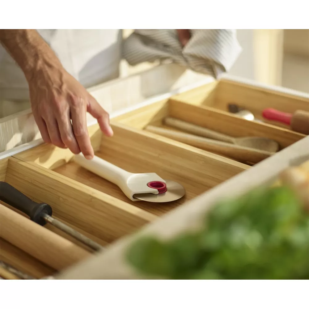 Una mano toma un cortador de pizza en un cajón de madera con utensilios.