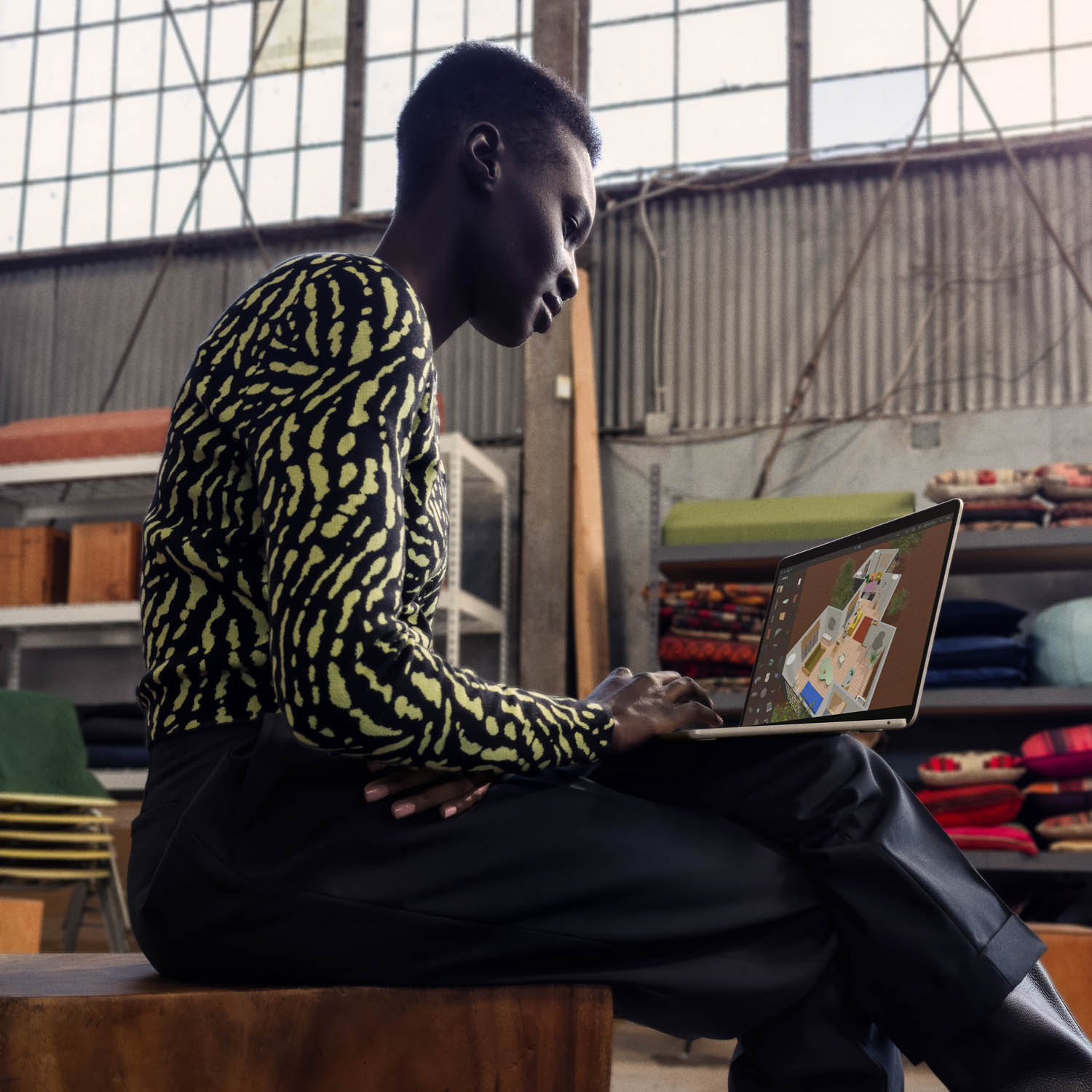 Una persona dalla pelle scura è seduta e usa un laptop che mostra un progetto di planimetria.