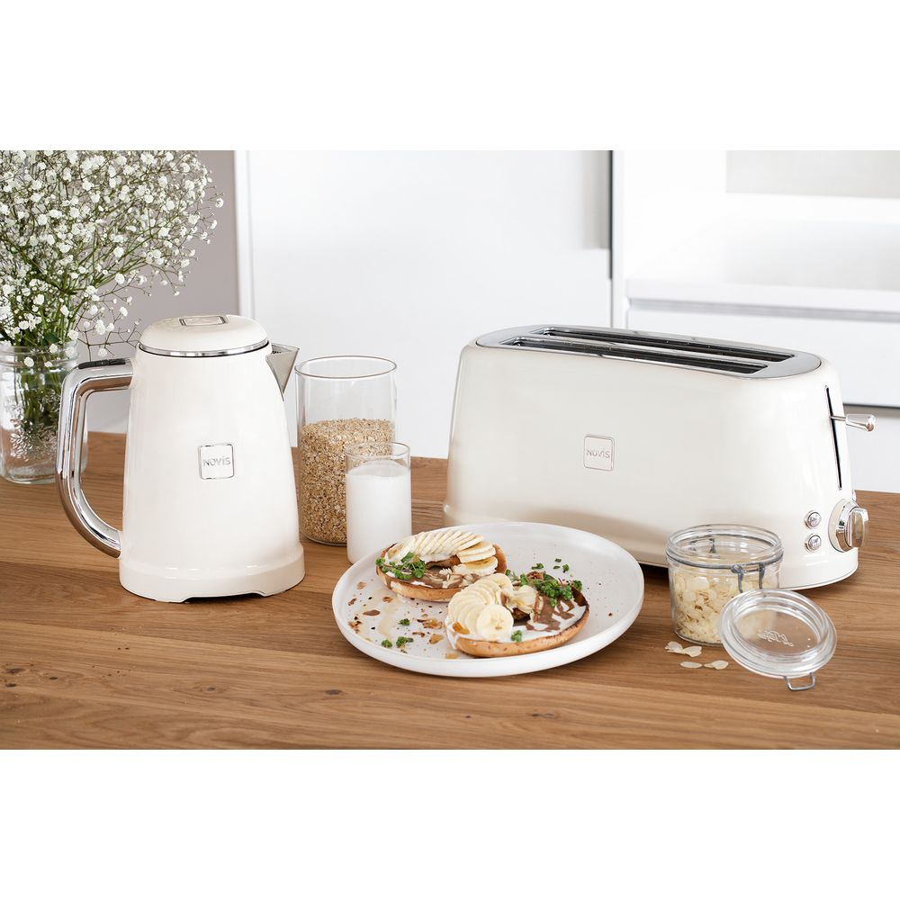Ein cremefarbener Wasserkocher, Toaster, Müsli und Bagels mit Bananen auf einem Holztisch.