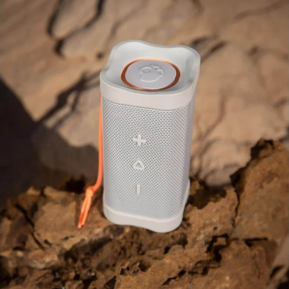 Ein weißer Lautsprecher mit orangem Band auf Felsen.