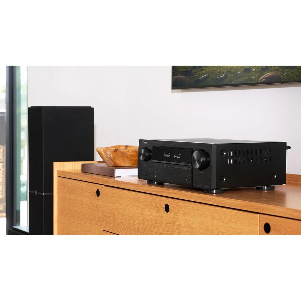 Schwarzer AV-Receiver auf einem Holzschrank mit Lautsprecher und Kunst.