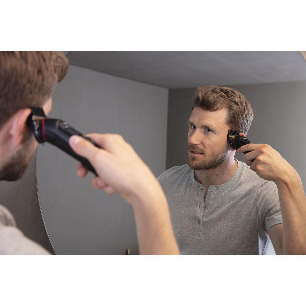 Man trimt haar in spiegel met tondeuse.