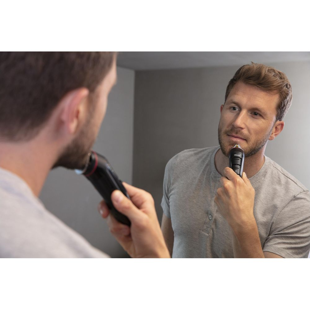 Een man scheert zijn baard in de spiegel met een elektrische trimmer.