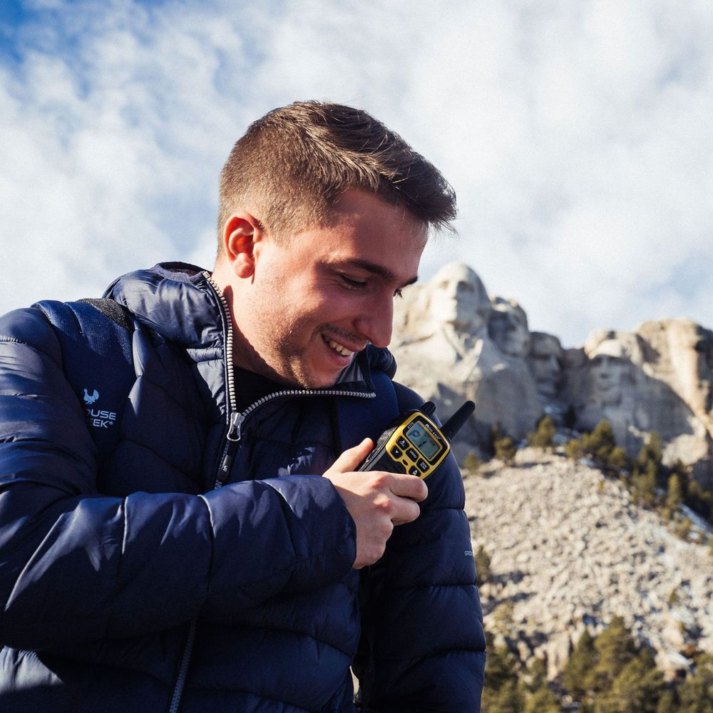 Uomo con walkie-talkie davanti a Mount Rushmore, cielo blu.