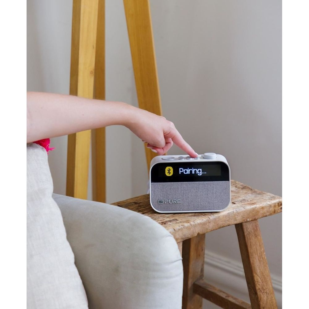 Una mano presiona una radio que muestra "Pairing...". 