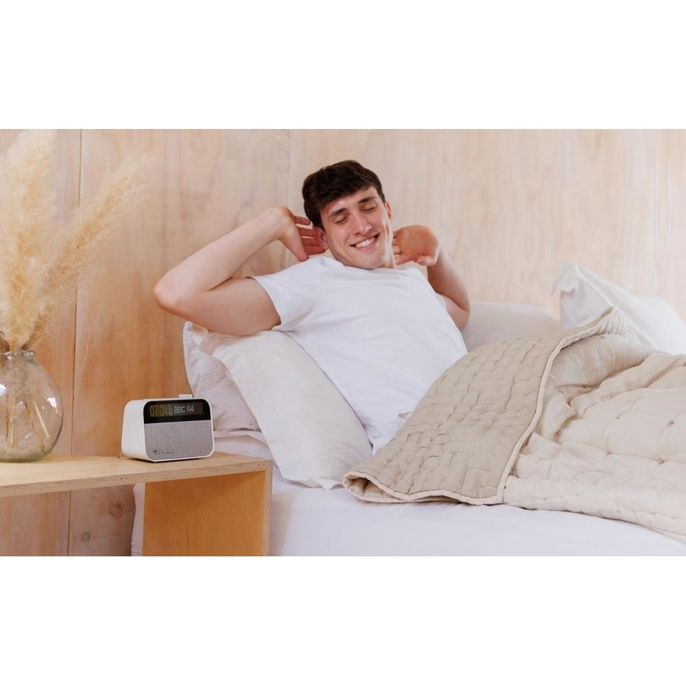 Hombre estirándose en la cama, con un radio despertador al lado.
