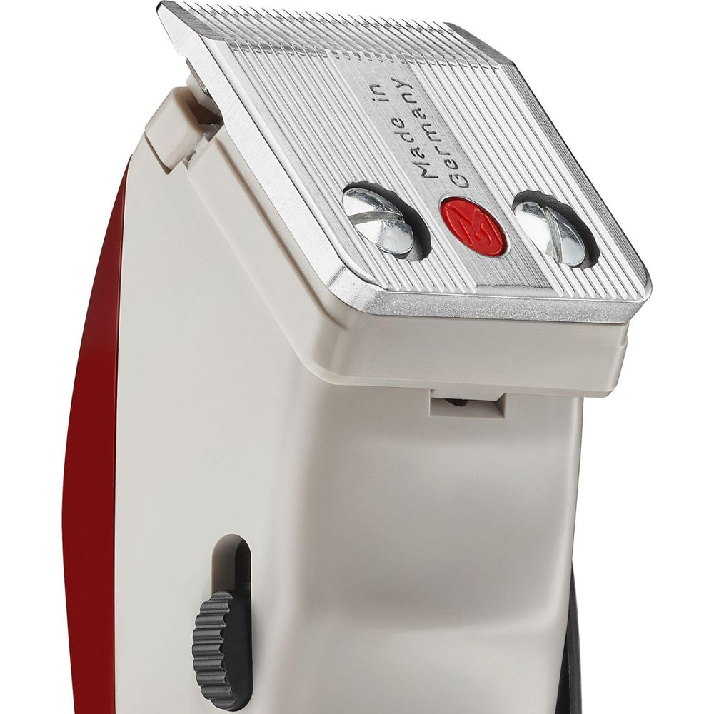 Zbliżenie maszynki do strzyżenia włosów z metalowym ostrzem, czerwonym przyciskiem i szarą obudową.