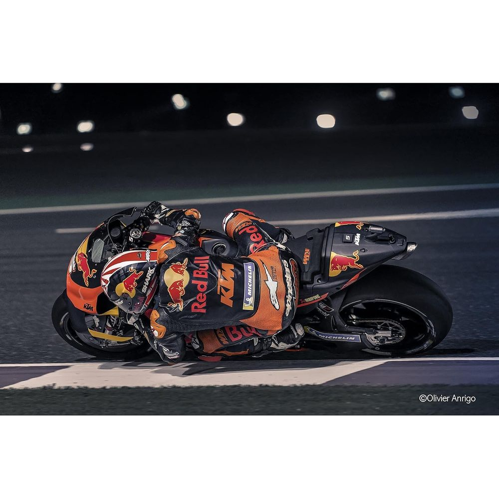 Rennfahrer in orange-schwarzer Kleidung auf einem Motorrad bei Nacht.