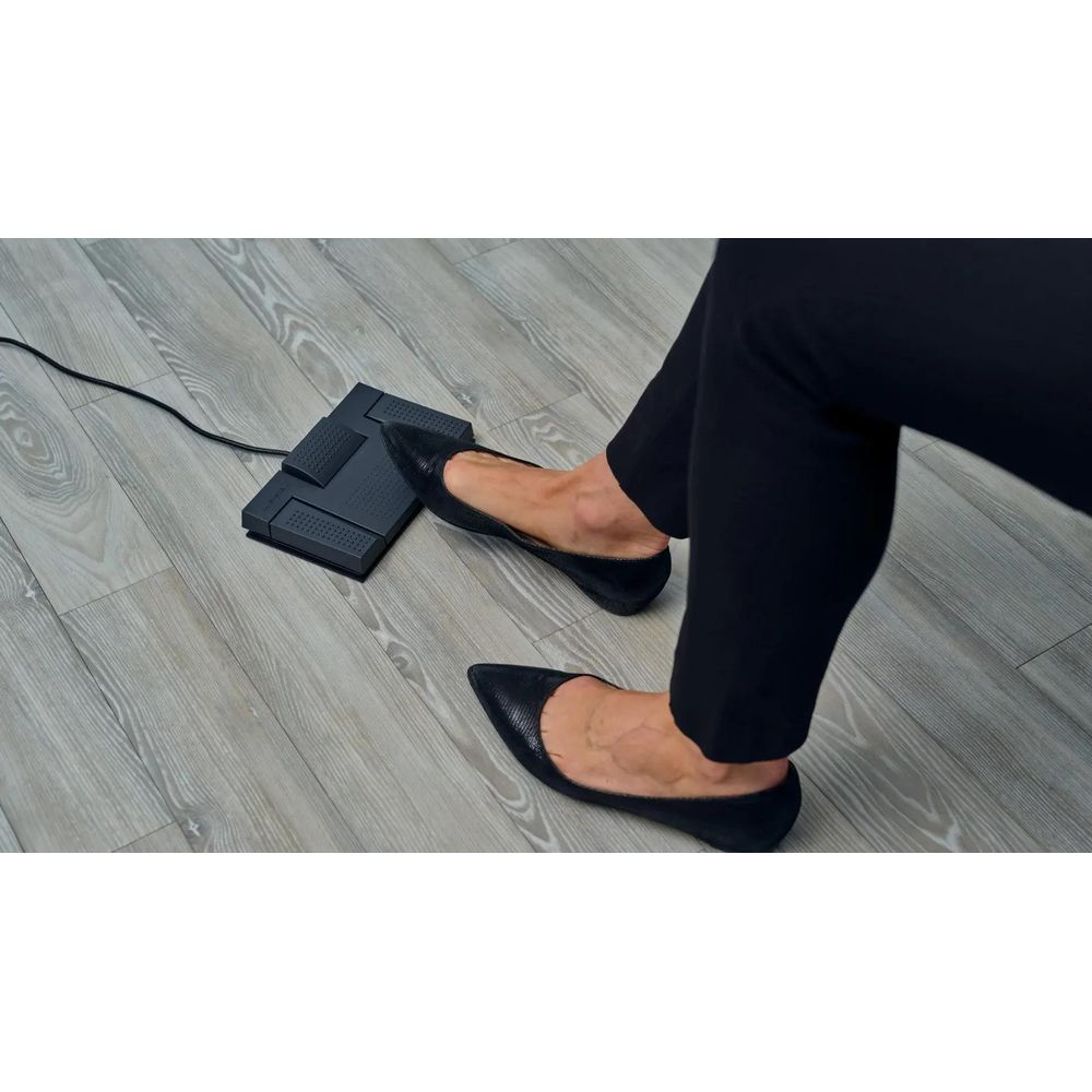 Füße in schwarzen flachen Schuhen auf einem Holzboden neben einem schwarzen Fußpedal.