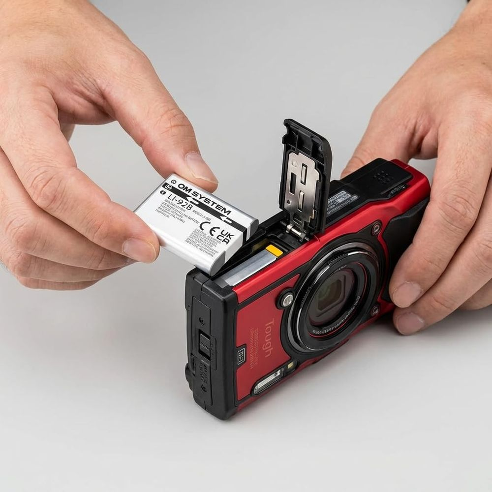 Hände setzen eine Kamera-Batterie in eine rote Kamera ein.