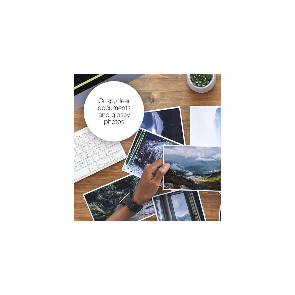 Dłoń trzyma zdjęcie górskie na drewnianym biurku ze zdjęciami i klawiaturą.