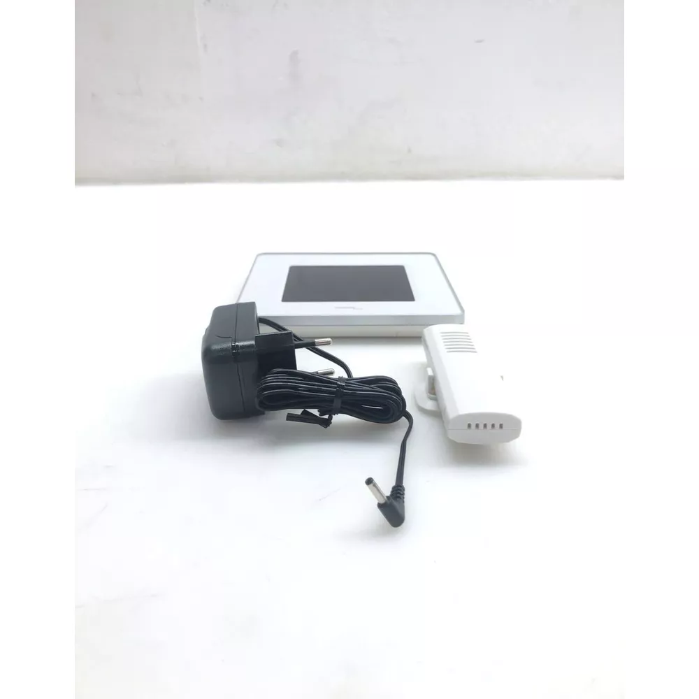Ein schwarzer Netzstecker mit Kabel, ein weißes Gerät und ein weißes Panel mit schwarzem Bildschirm.
