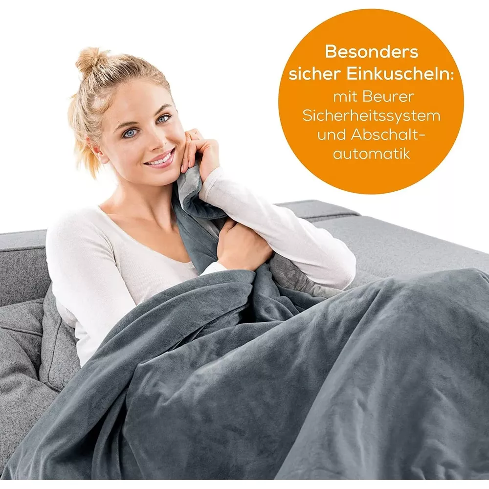 A woman snuggles in a gray blanket on a sofa, smiling.