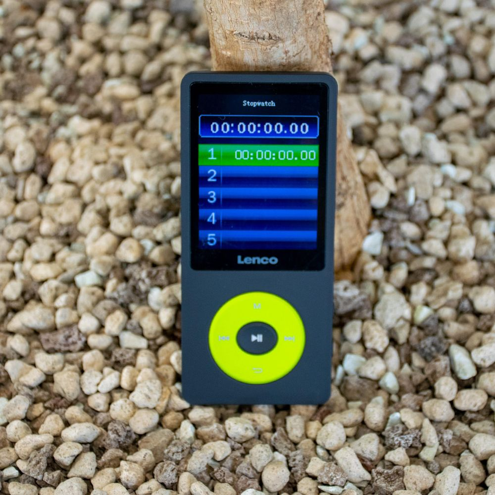 Un lecteur MP3 Lenco gris avec écran chronomètre sur gravier.