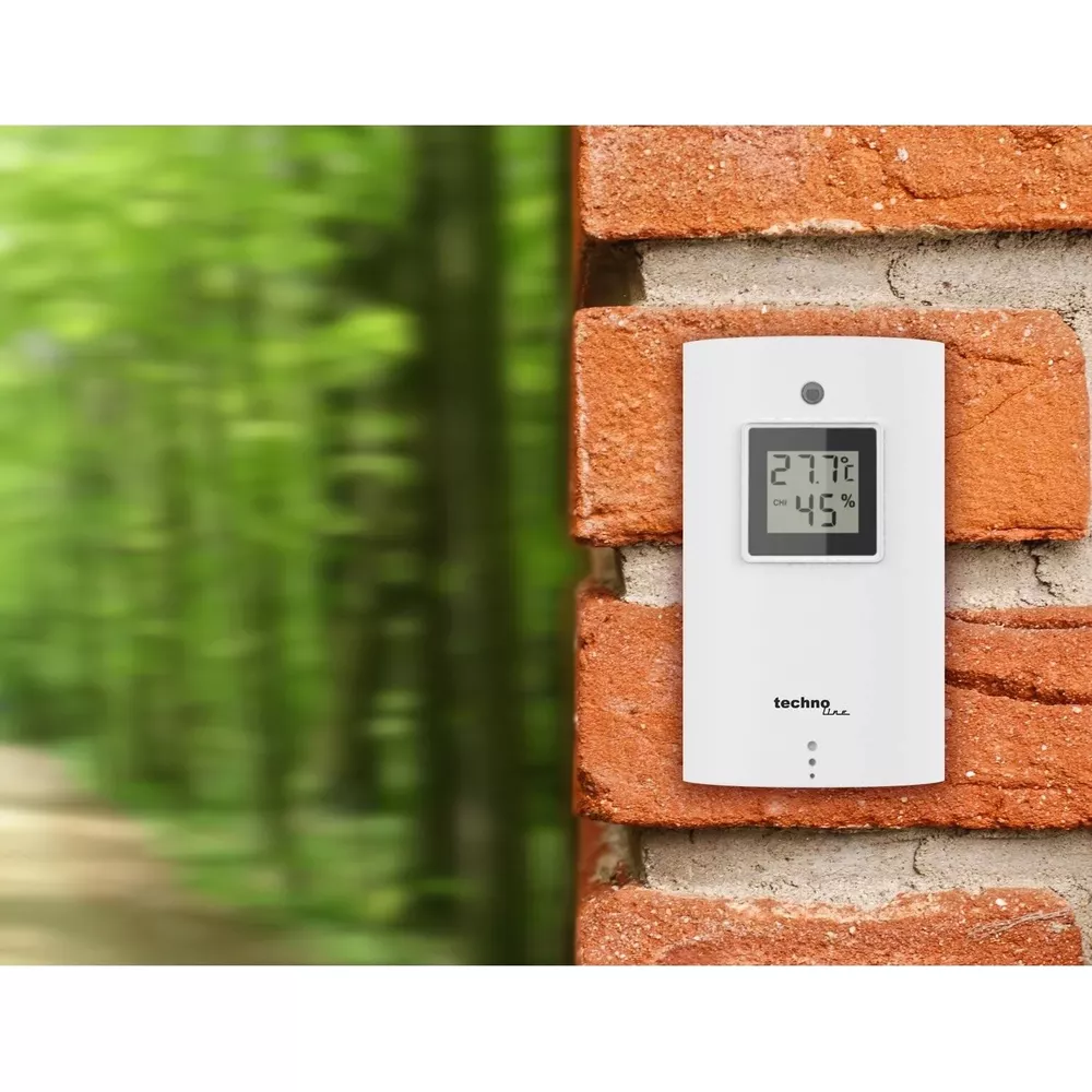 Un appareil météo blanc affiche 27.7C et 45% d'humidité sur un mur de briques.