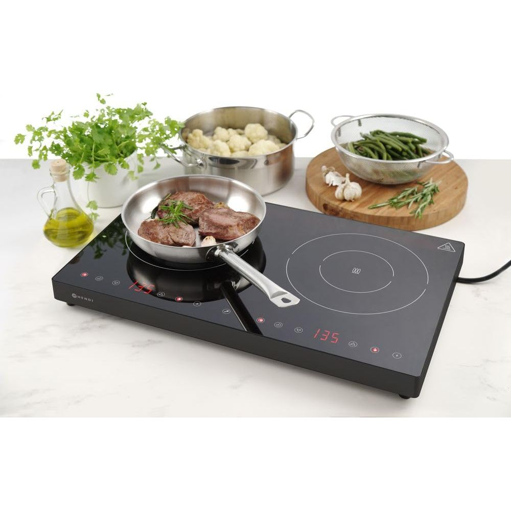 Un piano cottura a induzione con carne in padella, cavolfiore, fagioli e olio.