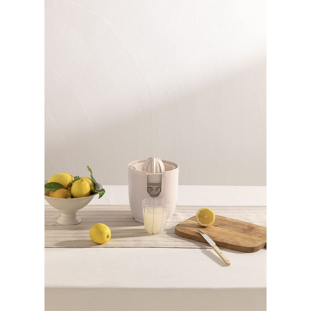 Un exprimidor con limones, un vaso de jugo y una tabla de cortar.