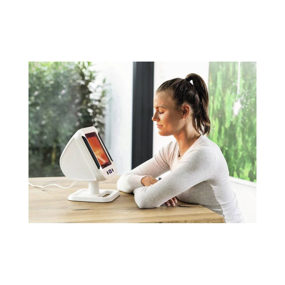 Woman sitting in front of a light therapy lamp at a wooden table.