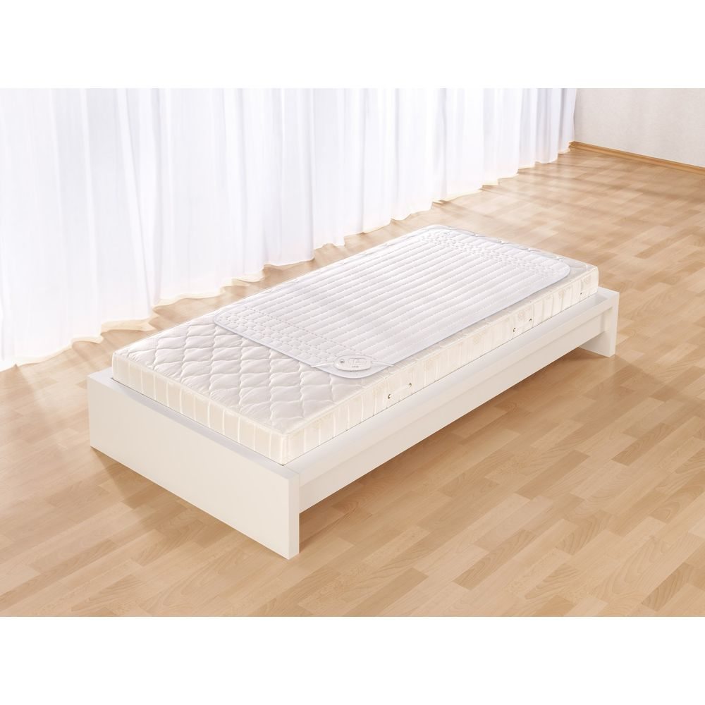 Un letto bianco con materasso e topper bianco, su pavimento in legno.