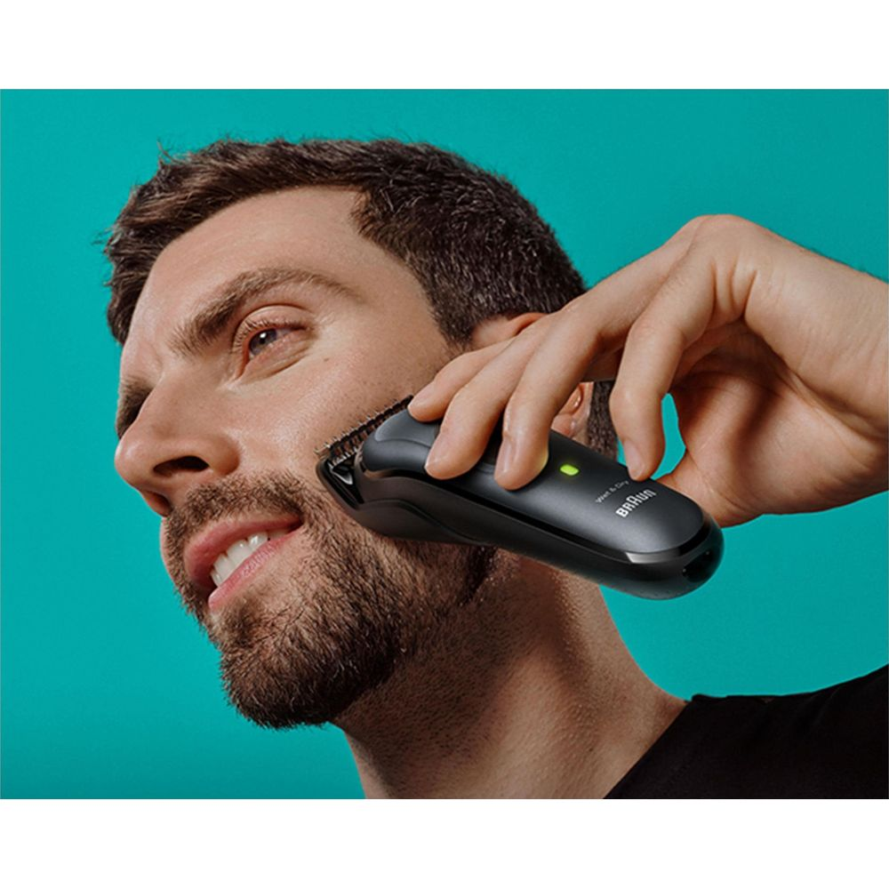 Mężczyzna przycina brodę czarną maszynką Braun. Jasne tło.