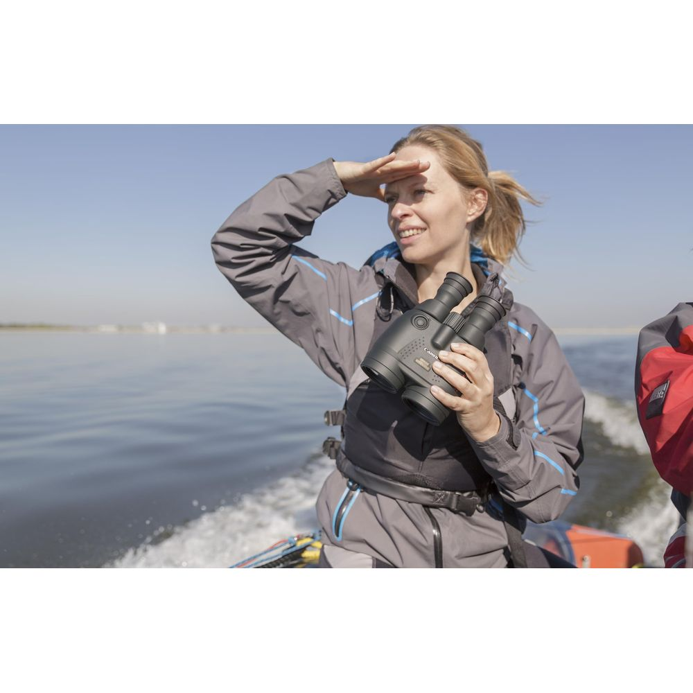 Kobieta na łodzi trzyma lornetkę, patrzy na wodę.