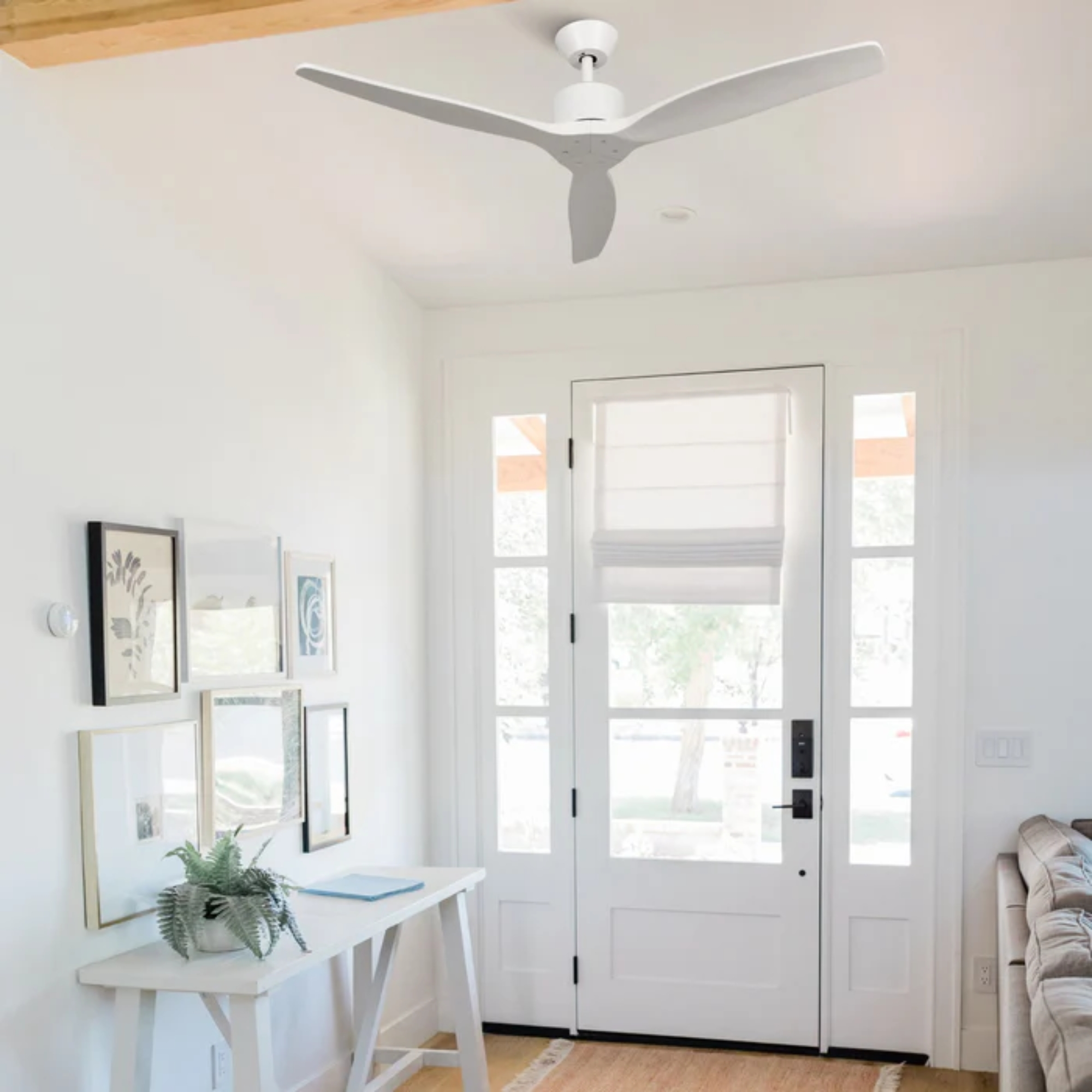 Un ventilador de techo blanco moderno sobre una consola blanca con arte enmarcado.