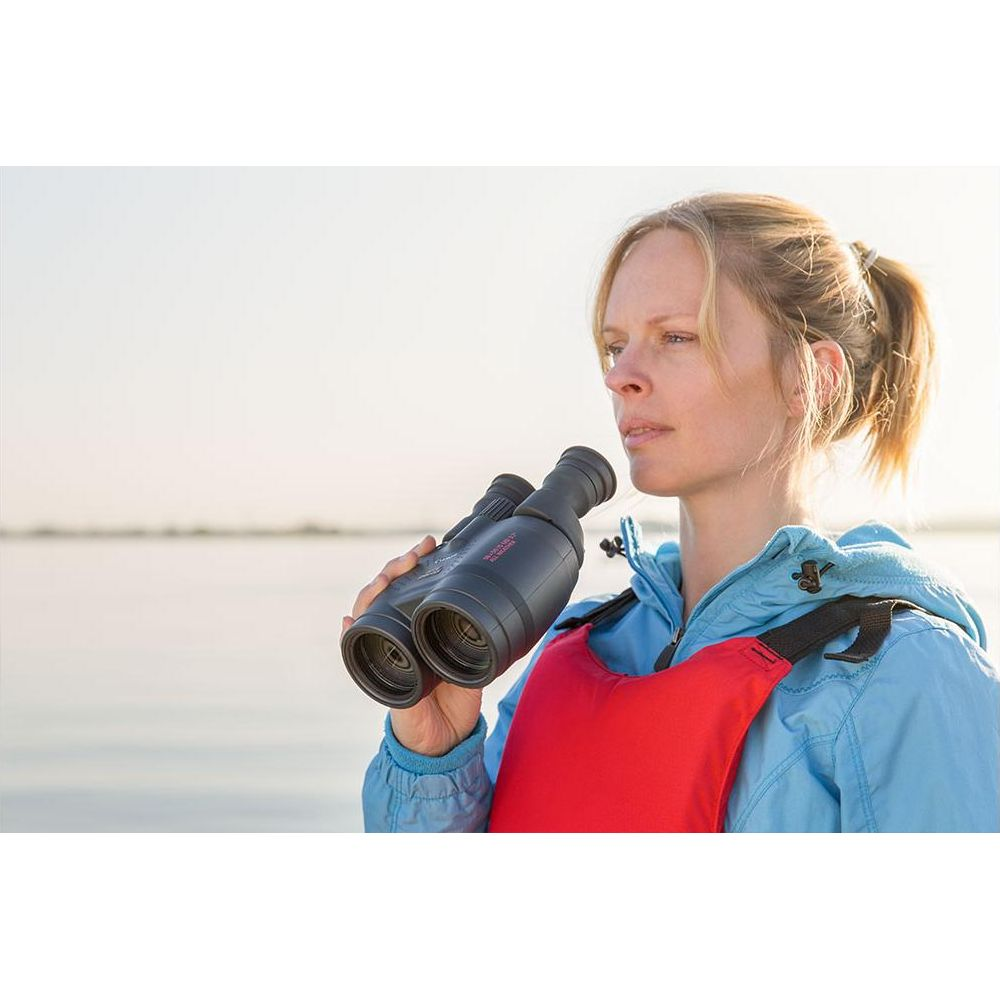 Frau mit Fernglas, trägt eine rote Schwimmweste und blaue Jacke.