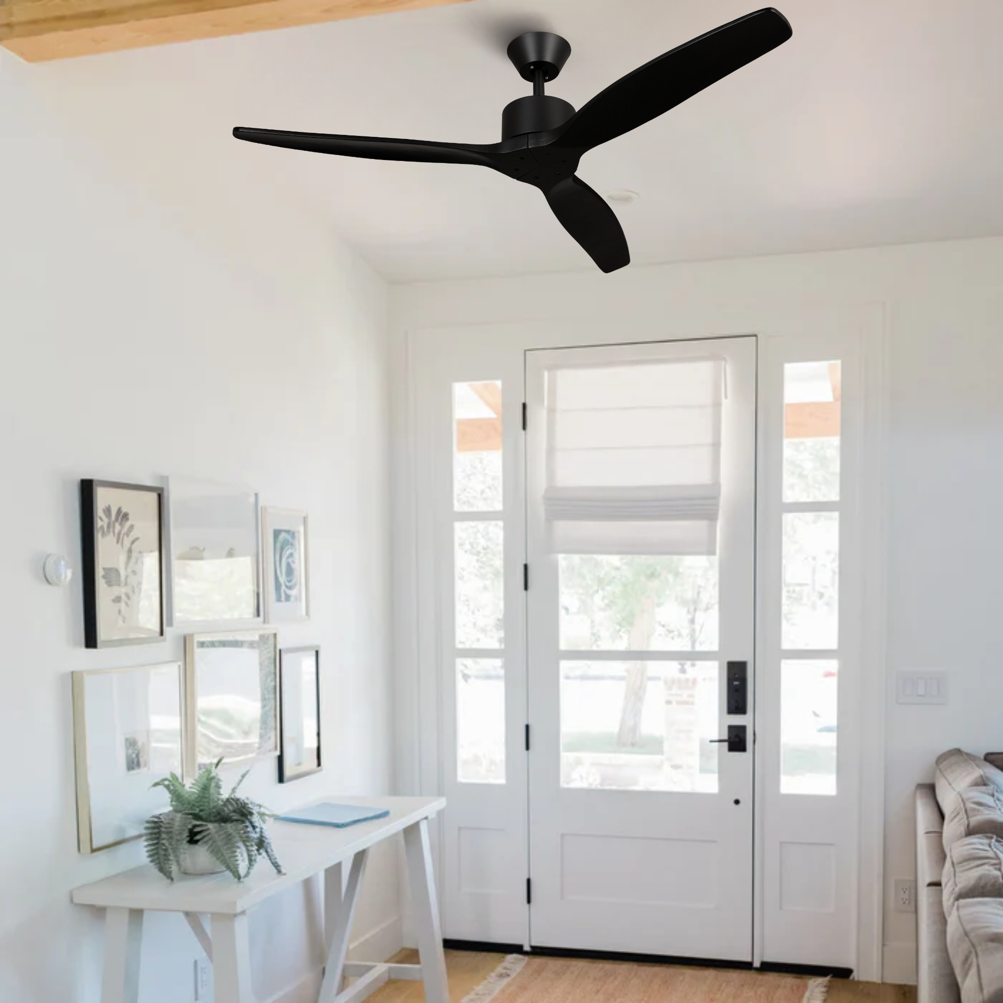 Ventilador de techo negro sobre una consola blanca con cuadros y una planta.