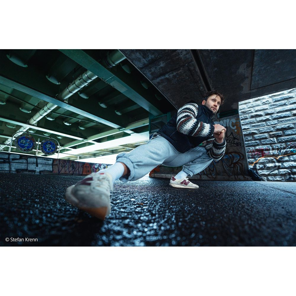 Man in athletic wear crouches under a bridge on wet ground.