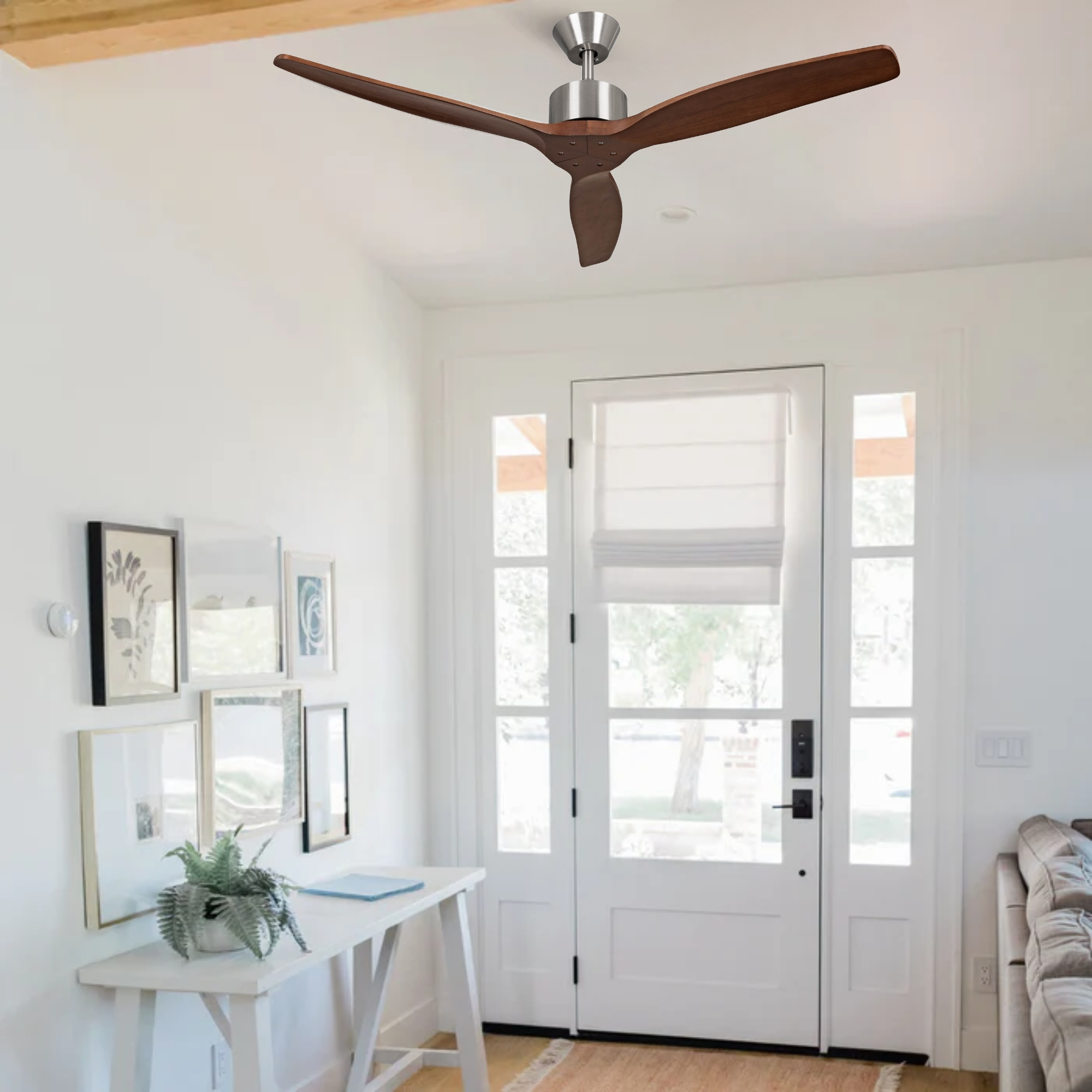 Un ventilador de techo moderno con aspas de madera oscura cuelga sobre una mesa consola blanca con arte enmarcado.