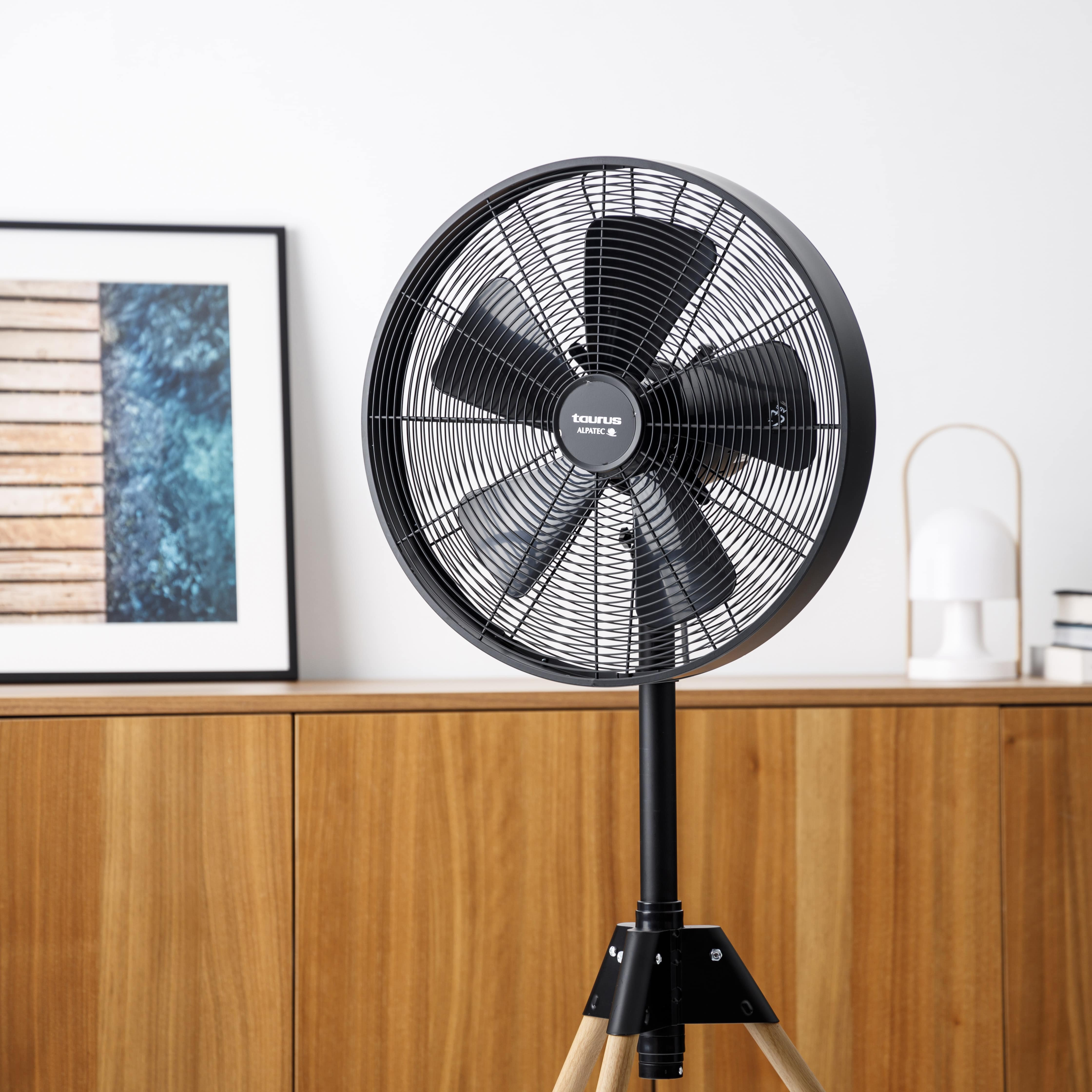 Un ventilador de pie negro con patas de madera frente a un armario de madera.