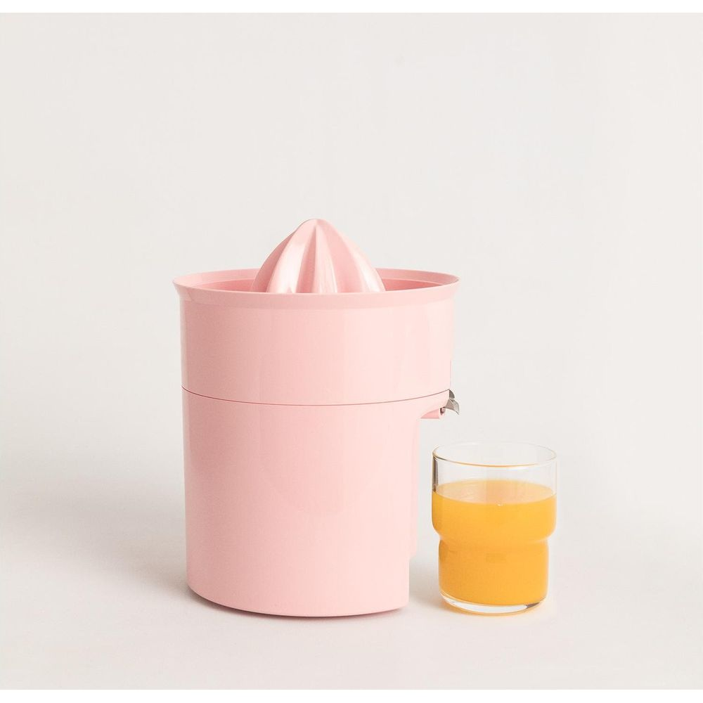 Un spremiagrumi rosa e un bicchiere di succo d'arancia su sfondo bianco.