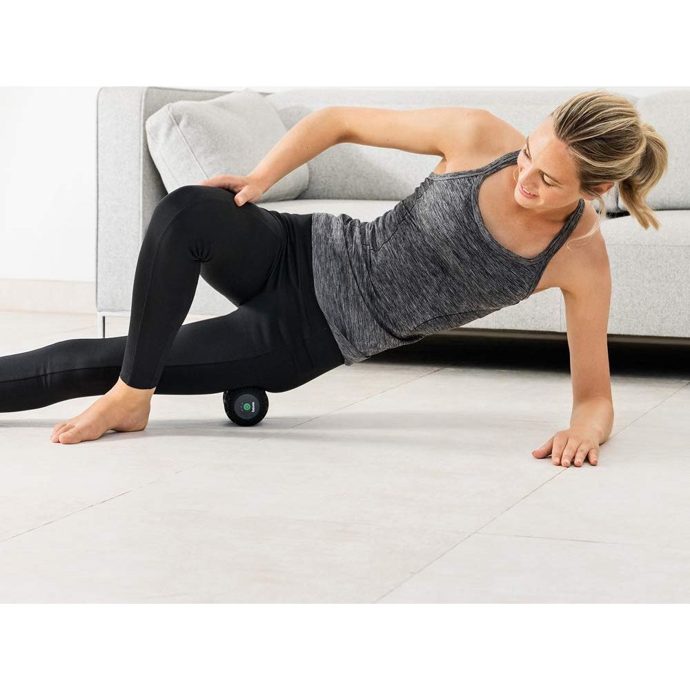 Frau rollt ihren Oberschenkel auf einem schwarzen Massageball auf dem Boden.