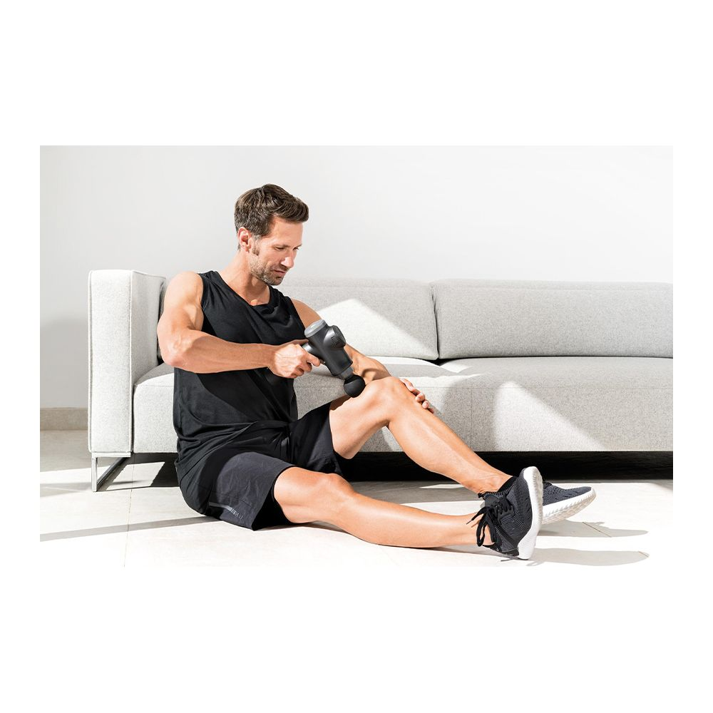 Mann sitzt auf dem Boden und massiert sein Bein mit einer Massagepistole.