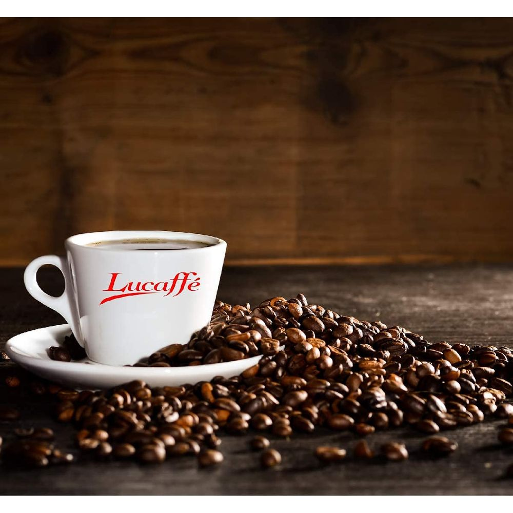 Eine weiße Tasse mit Kaffee steht auf einer Untertasse, umgeben von Kaffeebohnen.