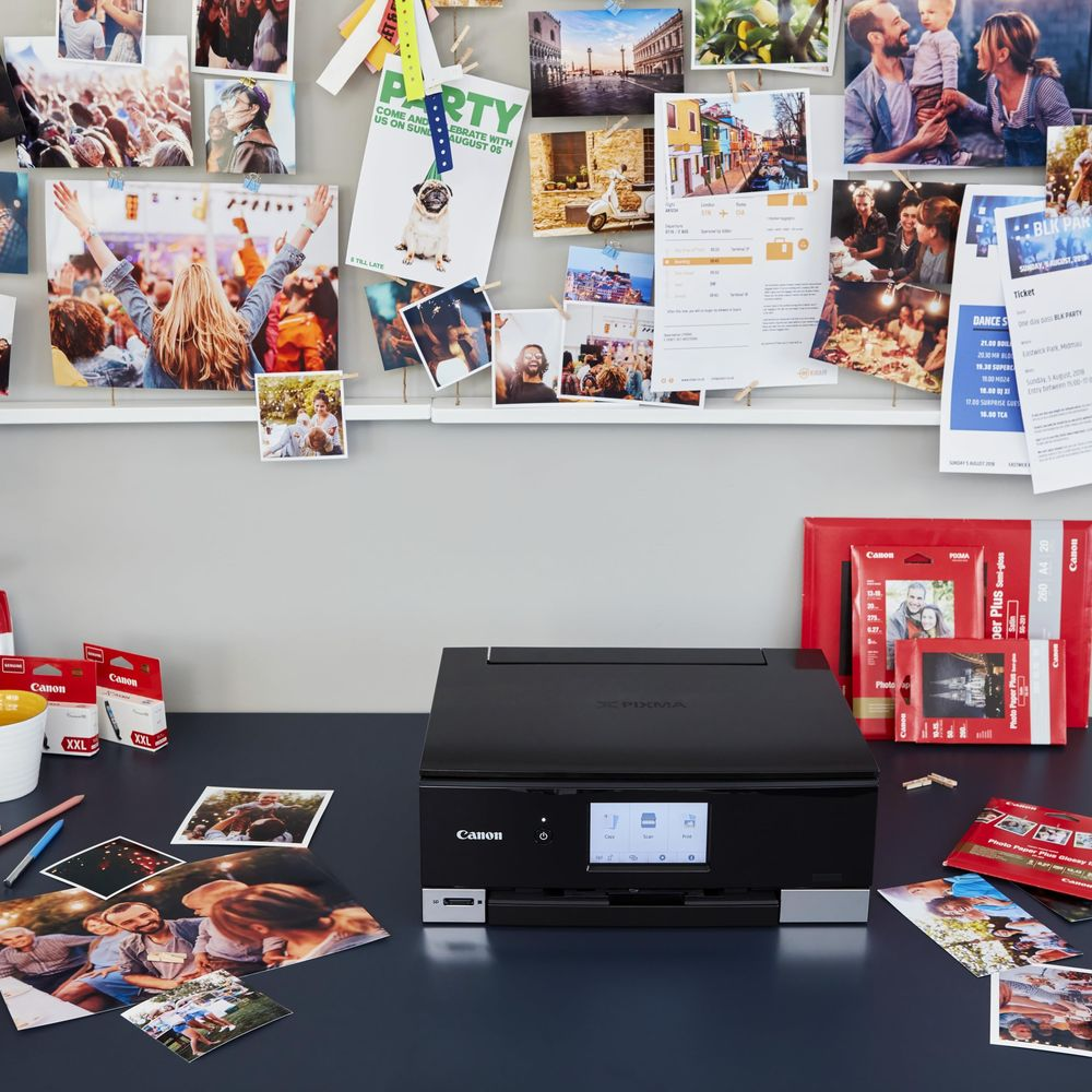 Czarna drukarka Canon na biurku ze zdjęciami i akcesoriami do drukarki.
