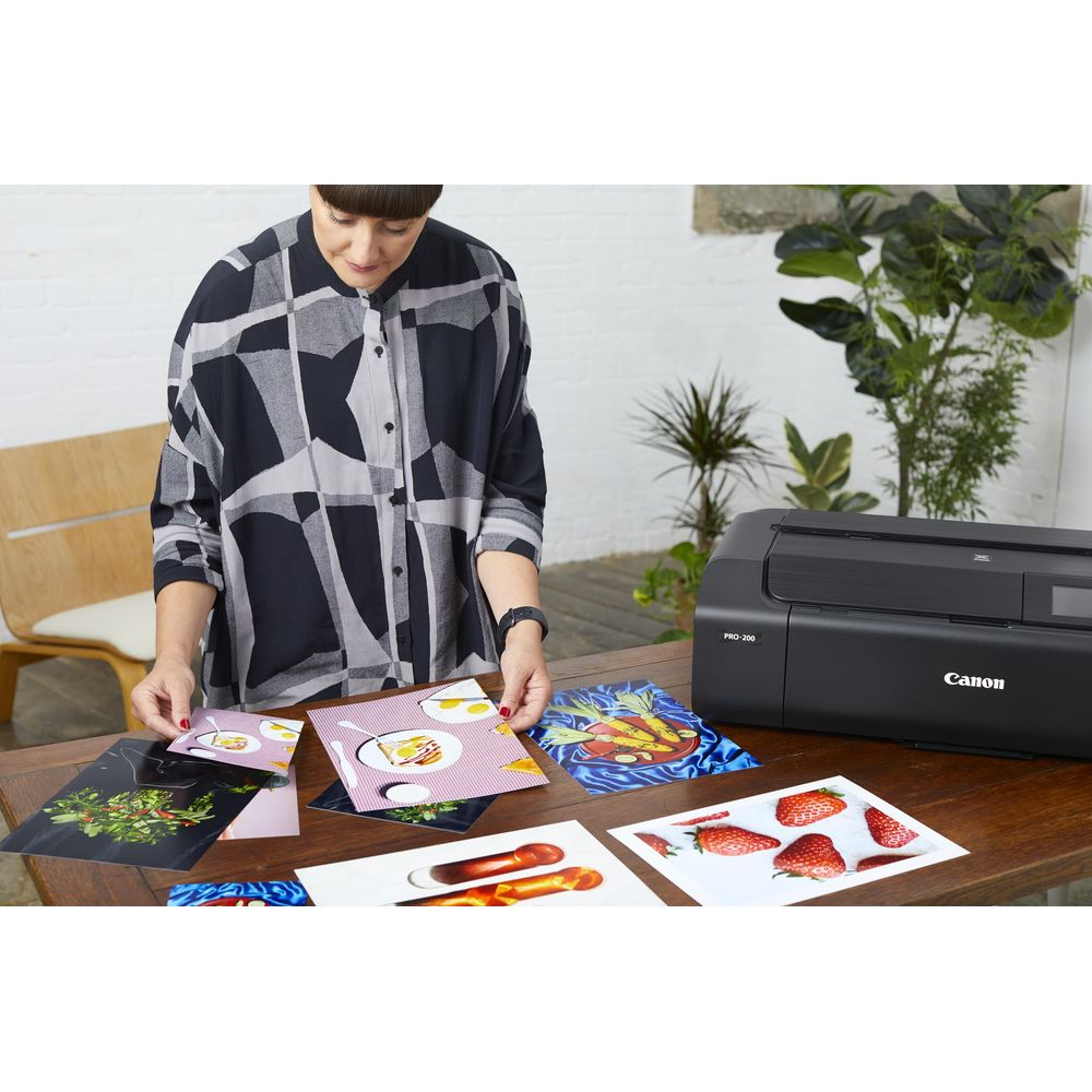 Kobieta sortuje zdjęcia obok drukarki Canon na drewnianym stole.