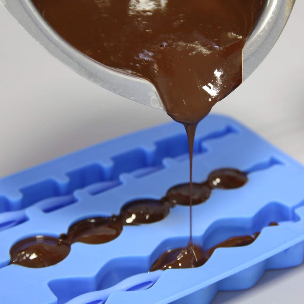 Flüssige Schokolade wird aus einem Topf in eine blaue Silikonform gegossen.