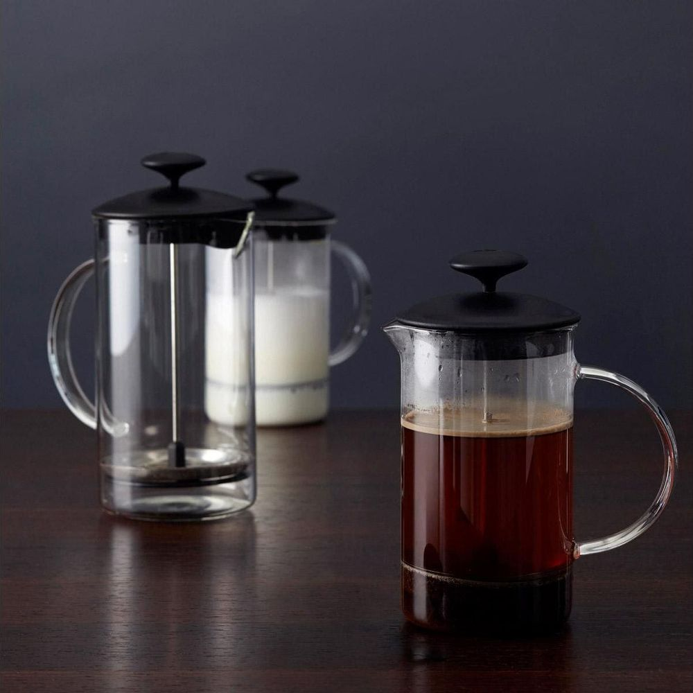 Drei Glas-French-Press-Kaffeemaschinen mit schwarzen Deckeln auf einem Holztisch.