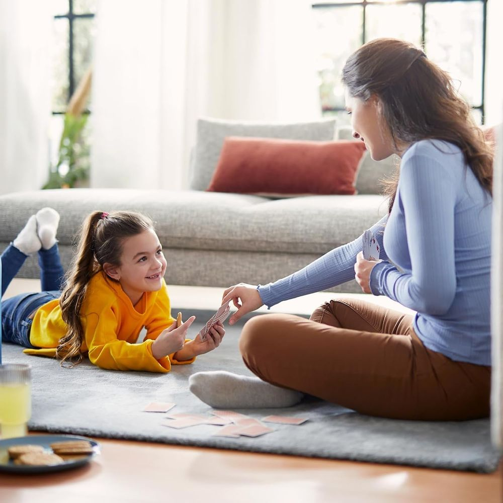 Mutter und Tochter spielen Karten auf dem Teppich im Wohnzimmer.