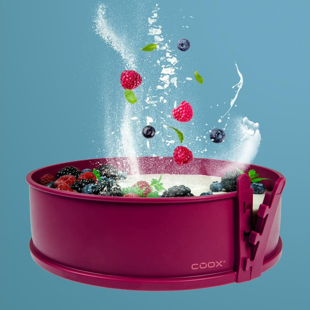 Himbeeren und Blaubeeren fallen in eine rosa Kuchenform mit Puderzucker.