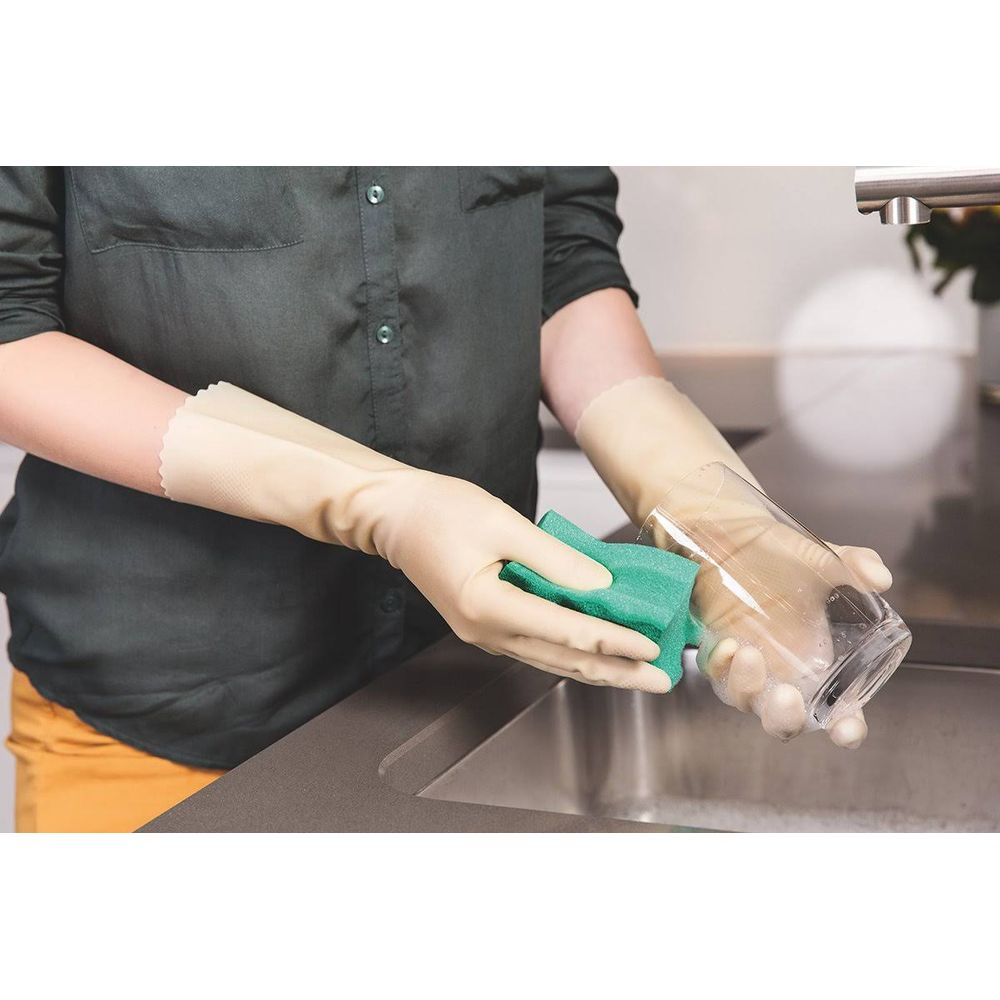 Person mit beige Handschuhen spült ein Glas mit einem grünen Schwamm.