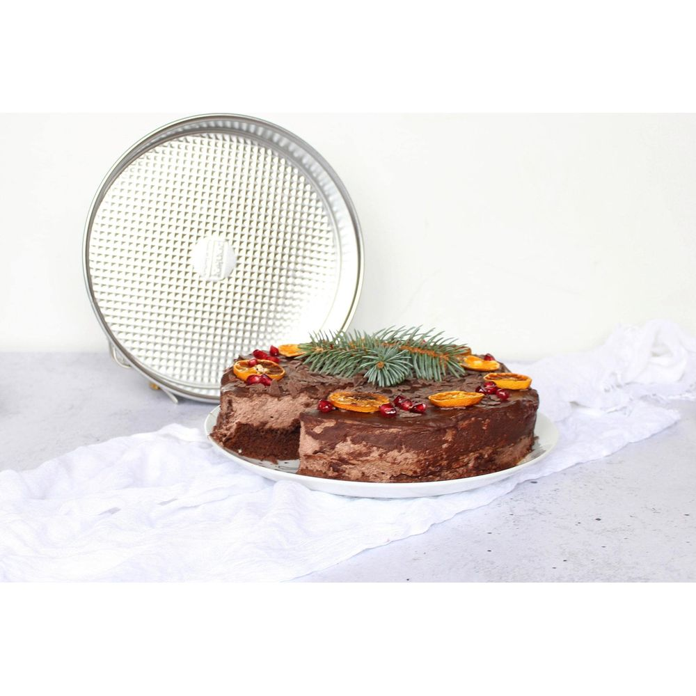 Schokoladenkuchen mit Orangenscheiben und Granatapfelkernen, neben einer Tortenform.