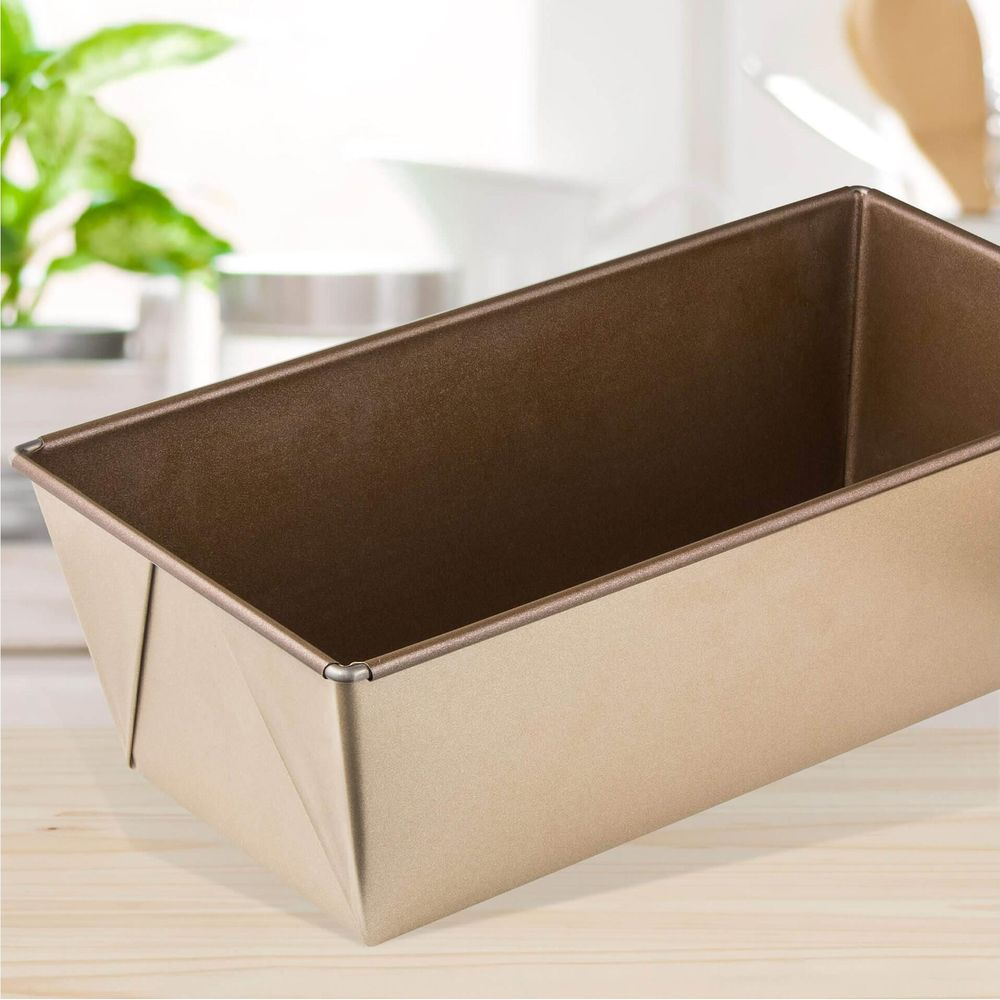 Eine goldfarbene rechteckige Kuchenform auf einem Holztisch, mit Pflanzen im Hintergrund.