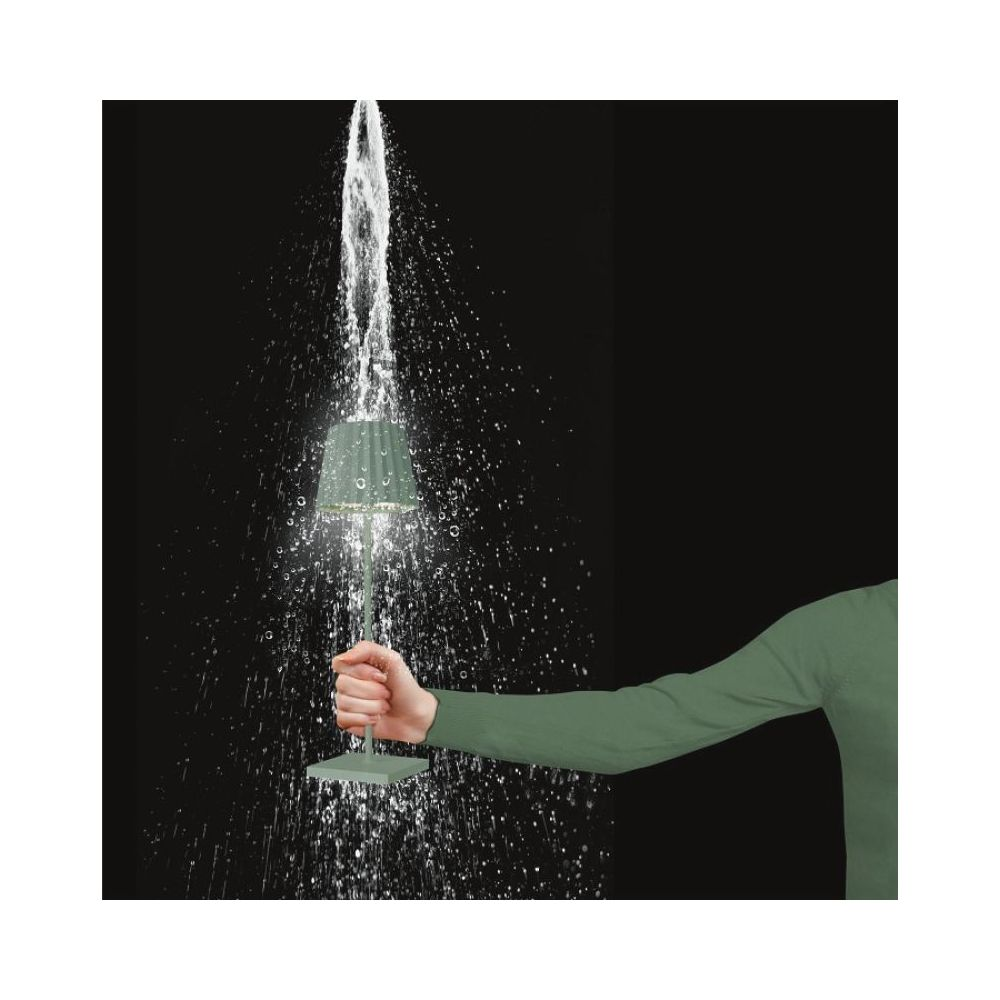 Una lampada verde tenuta sotto un getto d'acqua. Gocce d'acqua schizzano.