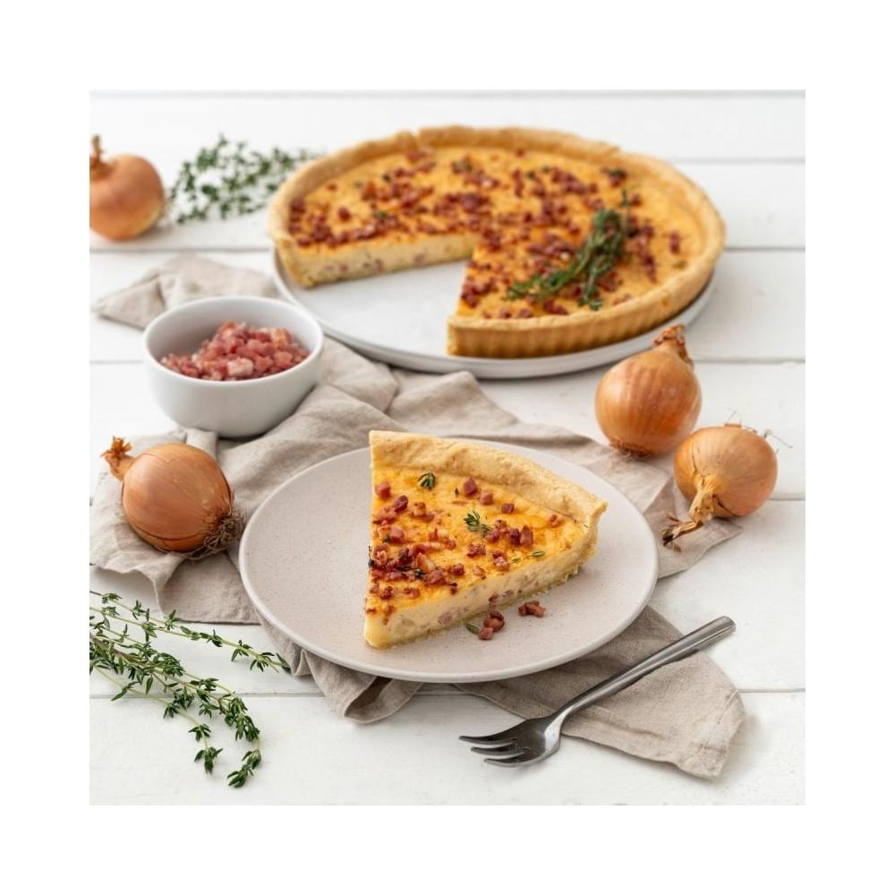 Ein Quiche-Stück auf einem Teller mit Zwiebeln und Kräutern auf einem Holztisch.