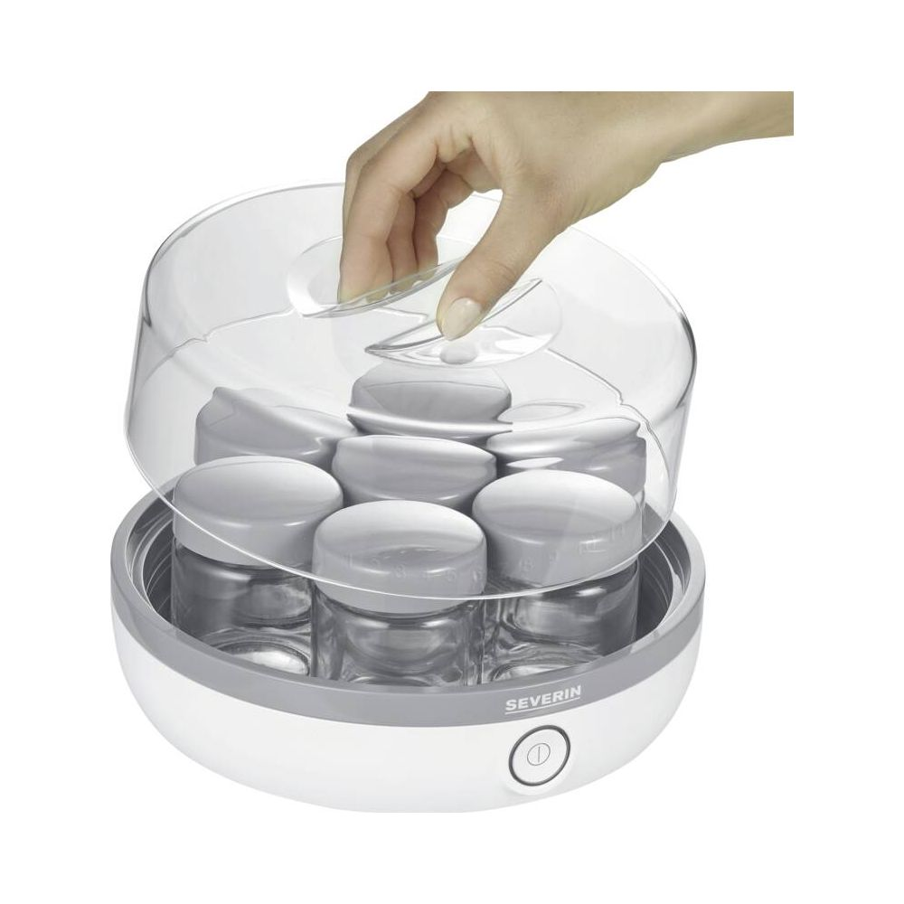 Ręka otwiera pokrywkę jogurtownicy z sześcioma słoiczkami.